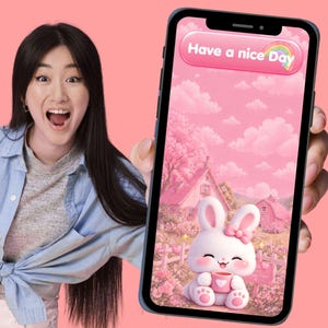 May include: A smartphone displays a pink screen with a cartoon bunny holding a cup, set against a pink landscape with the text "Have a nice Day". The phone is held by a person in a blue shirt.
