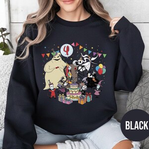 May include: Black sweatshirt featuring a colorful graphic of characters from The Nightmare Before Christmas celebrating a birthday. The design includes a cake, presents, and the number 4. The word "BLACK" is printed on a black circle.