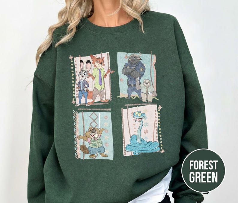 K&ouml;nnte beinhalten: Forstgr&uuml;nes Sweatshirt mit vier gerahmten Bildern von Zootopia-Charakteren. Die Charaktere sind Judy Hopps, Nick Wilde, Chief Bogo, Flash und andere. Das Sweatshirt hat eine einfarbige forstgr&uuml;ne Farbe.