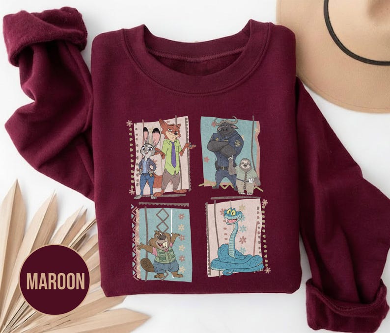 K&ouml;nnte beinhalten: Ein weinrotes Sweatshirt mit einem farbenfrohen Grafikdesign von Zeichentrickfiguren. Die Grafik ist in vier Felder unterteilt, die jeweils eine andere Figur zeigen. Das Wort "MAROON" ist auf einem kreisf&ouml;rmigen Etikett aufgedruckt.