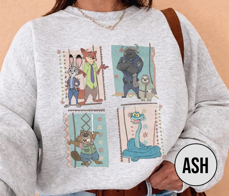 K&ouml;nnte beinhalten: Ein hellgraues Sweatshirt mit einem farbenfrohen Grafikdesign von Zeichentrickfiguren. Das Design umfasst vier rechteckige Tafeln mit Bildern eines Kaninchens, Fuchses, Bullen, Faultiers, Bibers und einer Schlange. Das Wort "ASH" befindet sich in einem Kreis unten rechts.