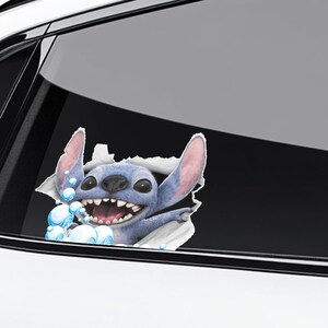 Puede incluir: Adhesivo para coche con el personaje Stitch, rompiendo una superficie rasgada. El personaje azul, con grandes orejas y una amplia sonrisa, est&aacute; rodeado de burbujas. Un art&iacute;culo decorativo y divertido.