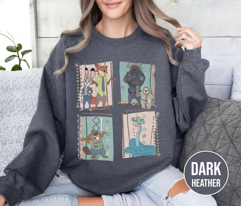 K&ouml;nnte beinhalten: Dunkelgraues Sweatshirt mit einem farbenfrohen Grafikdesign von Zeichentrickfiguren. Das Design umfasst vier rechteckige Tafeln mit verschiedenen Charakteren. Das Sweatshirt hat einen Rundhalsausschnitt und lange &Auml;rmel.