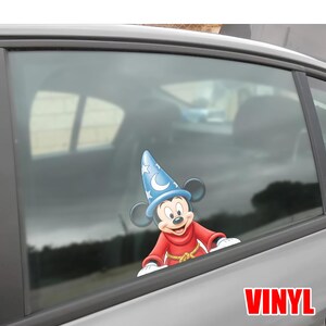 May include: A vinyl decal of Mickey Mouse in a sorcerer's outfit, with a blue hat adorned with stars and a crescent moon. The character is wearing a red robe with a gold rope belt. The word "VINYL" is printed in red.