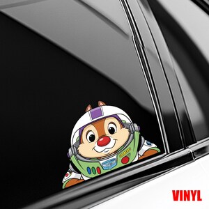 May include: A colorful vinyl decal featuring a cartoon chipmunk character wearing a Buzz Lightyear-inspired space suit and helmet. The decal is designed to be applied to a car window. The word "VINYL" is printed in red.