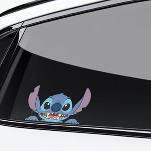 May include: A blue and purple cartoon character sticker, featuring large ears and a wide grin, is applied to a car window. The sticker is a playful design, likely for a vehicle, and adds a touch of personality.