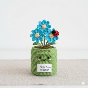 May include: A crocheted green pot with a smiling face holds three blue crocheted flowers with yellow centers and a red ladybug. A white tag on the pot reads "Thank You, Teacher."