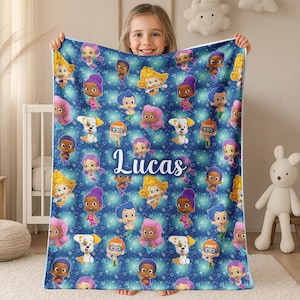 May include: A blue blanket featuring cartoon characters and the name "Lucas" in white script. The blanket has a pattern of various characters in different colors, set against a background of blue and white stars.