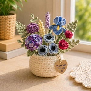 May include: A crocheted bouquet of colorful flowers in a cream-colored pot. The arrangement includes blue irises, red roses, purple hydrangeas, and other flowers. A heart-shaped tag reads "Thank you for all".