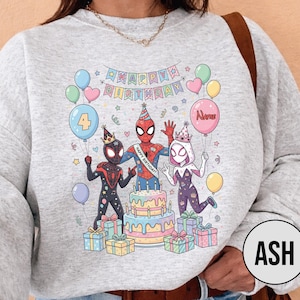 May include: A light gray sweatshirt featuring a colorful birthday design with Spider-Man characters, balloons, a cake, and wrapped gifts. The design includes the text "Happy Birthday" and a balloon with the word "Name".