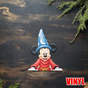 May include: A vinyl decal of Mickey Mouse in a sorcerer's hat and red robe. The blue hat has white stars and a crescent moon. The word "VINYL" is in red letters at the bottom right.