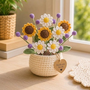 May include: A crocheted flower arrangement featuring sunflowers, daisies, and purple accents in a cream-colored pot. The arrangement includes a tag that reads "Thank you for all". The handmade flowers are displayed on a wooden surface.