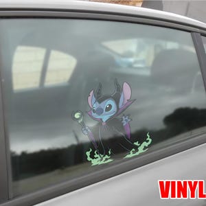 May include: A vinyl car window decal featuring a cartoon character, Stitch, dressed as Maleficent. The blue and purple character holds a staff and is surrounded by green flames. The word "VINYL" is printed in red.