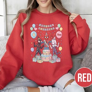 May include: A red sweatshirt featuring a colorful graphic of Spider-Man characters celebrating a birthday. The design includes a cake, balloons, and the words "Happy Birthday". The number "4" is also displayed.