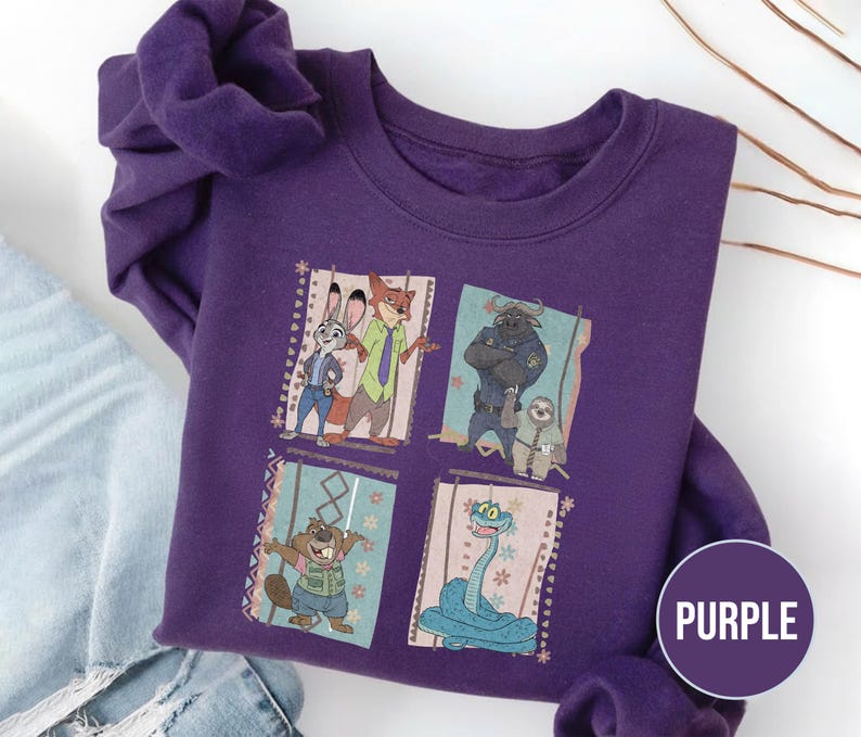K&ouml;nnte beinhalten: Ein lila Sweatshirt mit einer farbenfrohen Grafik von Charakteren aus dem Animationsfilm Zoomania. Das Design umfasst Judy Hopps, Nick Wilde, Chief Bogo, Flash und andere. Das Wort "PURPLE" befindet sich in einem lila Kreis.