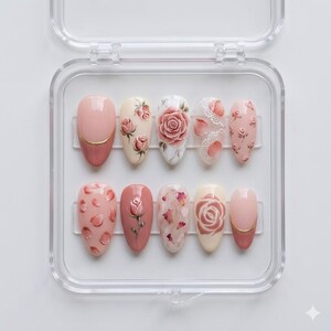 May include: A set of ten artificial nails in a clear plastic case. The nails feature various designs, including rose patterns, floral accents, and solid colors. The color palette includes shades of pink, white, and gold.