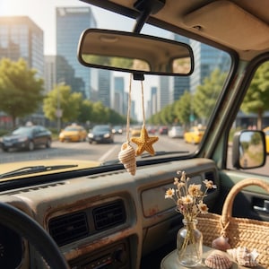 May include: Interior view of a vintage car with a city backdrop. A rearview mirror hangs above a crocheted seashell and starfish car charm. A small vase of dried flowers and a woven basket sit on the dashboard, with a city street in the background.