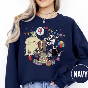 May include: Navy blue sweatshirt featuring a colorful graphic of characters from The Nightmare Before Christmas celebrating a birthday. The design includes a birthday cake, presents, and the number 4. The word "NAME" is also visible.