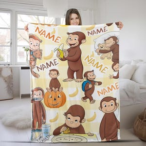 May include: A personalized blanket featuring a cartoon monkey character in various poses, set against a yellow and white checkered background. The blanket includes the word "NAME" and images of bananas and a pumpkin.