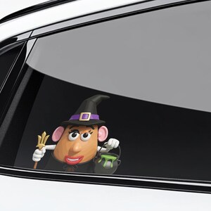 May include: A Halloween-themed car window decal featuring a cartoon potato character dressed as a witch. The character wears a black hat with a purple band, a black cape, and holds a trident and a cauldron with green slime.