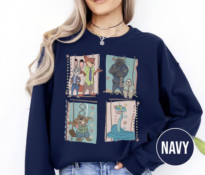 K&ouml;nnte beinhalten: Marineblaues Sweatshirt mit vier gerahmten Illustrationen von Zootopia-Charakteren. Die Illustrationen zeigen Judy Hopps, Nick Wilde, Chief Bogo, Flash, Mr. Big und eine Schlange. Das Wort "NAVY" ist in einem wei&szlig;en Kreis unten rechts aufgedruckt.