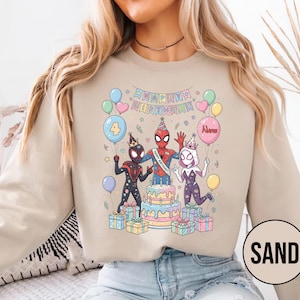 May include: Sand-colored sweatshirt featuring a colorful graphic of Spider-Man characters celebrating a birthday. The design includes a cake, balloons, and the text "Happy Birthday". The number "4" is on a balloon.