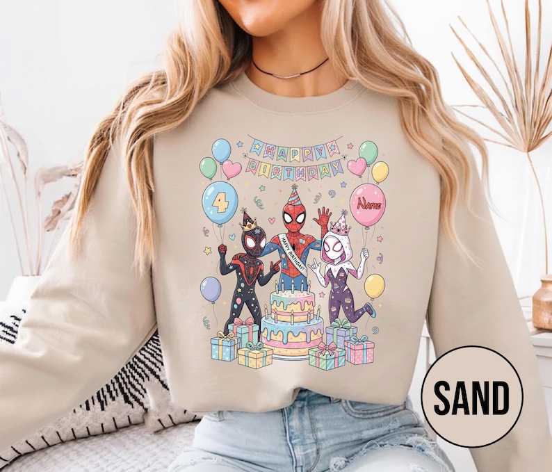 May include: Sand-colored sweatshirt featuring a colorful graphic of Spider-Man characters celebrating a birthday. The design includes a cake, balloons, and the text "Happy Birthday". The number "4" is on a balloon.