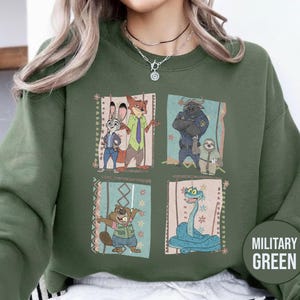 K&ouml;nnte beinhalten: Milit&auml;rgr&uuml;nes Sweatshirt mit einem Cartoon-Motiv von Charakteren aus einem Animationsfilm. Das Design zeigt ein Kaninchen, einen Fuchs, einen B&uuml;ffel, ein Faultier, einen Biber und eine Schlange. Das Sweatshirt hat einen Rundhalsausschnitt.