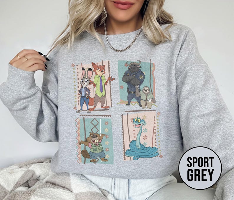 K&ouml;nnte beinhalten: Sportgraues Sweatshirt mit einem farbenfrohen Grafikdesign von Zootopia-Charakteren. Das Design umfasst Judy Hopps, Nick Wilde, Chief Bogo, Flash und andere. Das Sweatshirt hat einen Rundhalsausschnitt und lange &Auml;rmel.