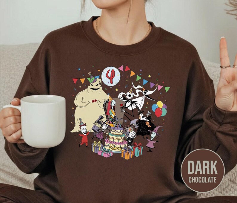 May include: Dark chocolate brown sweatshirt featuring a colorful graphic of characters from The Nightmare Before Christmas celebrating a birthday. The design includes a cake, balloons, and the number 4. The sweatshirt is a crew neck style.
