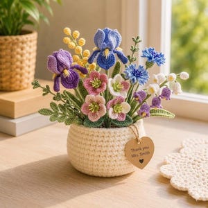 May include: A crocheted flower arrangement in a cream-colored pot. The bouquet includes purple irises, blue cornflowers, pink and white blossoms, and yellow mimosa. A heart-shaped tag reads "Thank you Mrs. Smith."