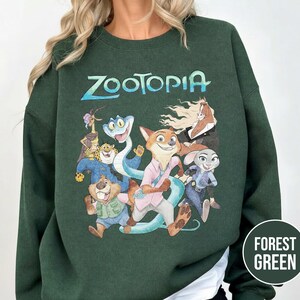 以下が含まれることがあります： アニメ映画のキャラクターのカラフルなグラフィックと「Zootopia」の文字がプリントされたフォレストグリーンのスウェットシャツ。スウェットシャツは無地のフォレストグリーンで、長袖です。