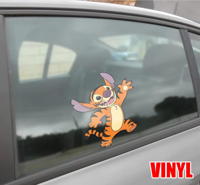 May include: Orange and tan vinyl decal of a cartoon character with large ears and a tiger-like pattern, waving with a cheerful expression. The decal is applied to a car window. The word "VINYL" is printed in red.