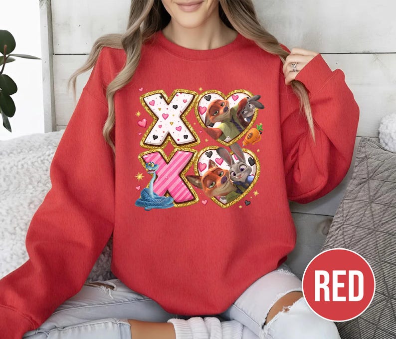 May include: A red sweatshirt featuring the text "XO" with heart and character graphics. The design includes cartoon characters within heart shapes, and a blue snake. The sweatshirt has a round neckline and long sleeves.