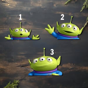 May include: Three green alien figures with three eyes, wearing blue and purple outfits. The figures are from the Toy Story franchise. Each figure has a different pose, with one figure waving, another with its arms out, and the last one looking straight ahead.