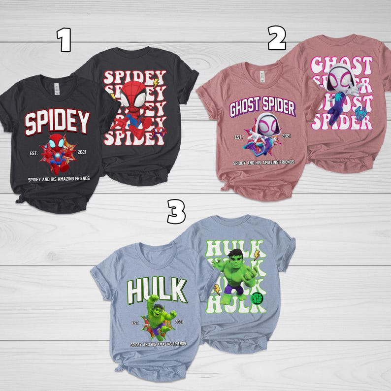Puede incluir: Tres camisetas de manga corta con gr&aacute;ficos de superh&eacute;roes. Las camisetas presentan las palabras "Spidey", "Ghost Spider" y "Hulk" con ilustraciones. Cada camiseta tiene el texto "Spidey and His Amazing Friends" y el a&ntilde;o "2021".