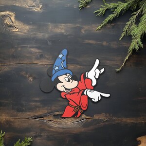 May include: A colorful wooden cutout of Mickey Mouse in a sorcerer's outfit. Mickey is wearing a blue hat with stars and a crescent moon, a red robe, and white gloves. The cutout is on a dark wood background.