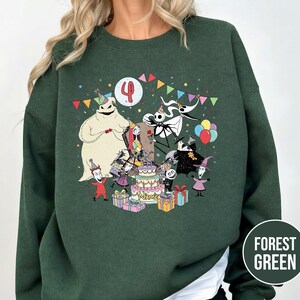 May include: Forest green sweatshirt featuring a colorful graphic of characters from The Nightmare Before Christmas celebrating a birthday. The design includes a birthday cake, presents, and the number 4.