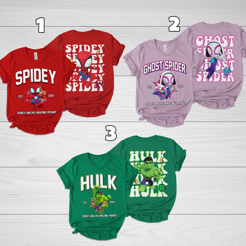 Puede incluir: Una colecci&oacute;n de tres camisetas de manga corta con gr&aacute;ficos de superh&eacute;roes. Las camisetas son rojas, lavanda y verdes. Las camisetas rojas dicen "Spidey" con un gr&aacute;fico de Spider-Man. Las camisetas lavanda dicen "Ghost Spider". Las camisetas verdes dicen "Hulk".