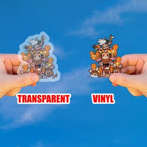 May include: Two stickers, one transparent and one vinyl, featuring a cartoon design of a group of characters with pumpkin and Halloween themes. The word "TRANSPARENT" is printed in red on the left, and "VINYL" is printed in red on the right.