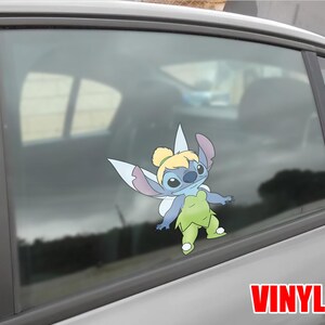 May include: A colorful vinyl decal of Stitch dressed as Tinkerbell, with blue, green, and purple hues. The decal is affixed to a car window. The word "VINYL" is printed in red at the bottom right.