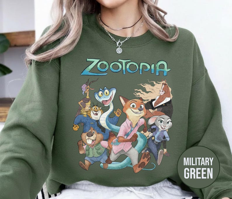 以下が含まれることがあります： 「Zootopia」の文字とアニメ映画のキャラクターのグラフィックが特徴のミリタリーグリーンのスウェットシャツ。デザインにはキツネ、ウサギ、ヘビ、その他の動物のキャラクターが含まれています。スウェットシャツは無地です。