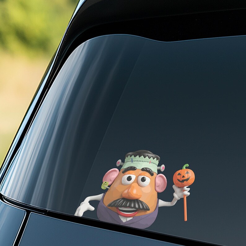 May include: A Halloween-themed car decal featuring a Mr. Potato Head character dressed as Frankenstein, holding an orange pumpkin on a stick. The decal is visible through a car window, with a blurred green background.