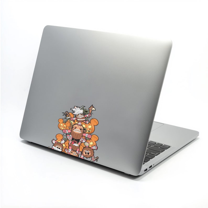 May include: A silver laptop with a colorful sticker featuring cartoon characters and orange pumpkins. The sticker is on the upper left corner of the laptop. The characters have various expressions and are in a pile.