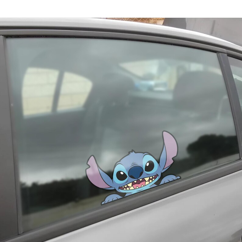 May include: A blue and purple cartoon character sticker, featuring large ears and a wide grin, is affixed to a car window. The sticker is a popular character from a Disney animated film.