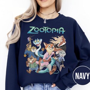 以下が含まれることがあります： ターコイズ色の「Zootopia」の文字と、アニメ映画のキャラクターのカラフルなグラフィックが特徴のネイビーブルーのスウェットシャツ。デザインにはキツネ、ウサギ、その他の動物のキャラクターが含まれています。スウェットシャツはクルーネックと長袖です。