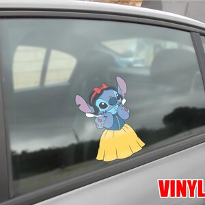 May include: A blue vinyl decal of Stitch dressed as Snow White, with a red bow, blue dress, and yellow skirt. The decal is applied to a car window. The word "VINYL" is printed in red.