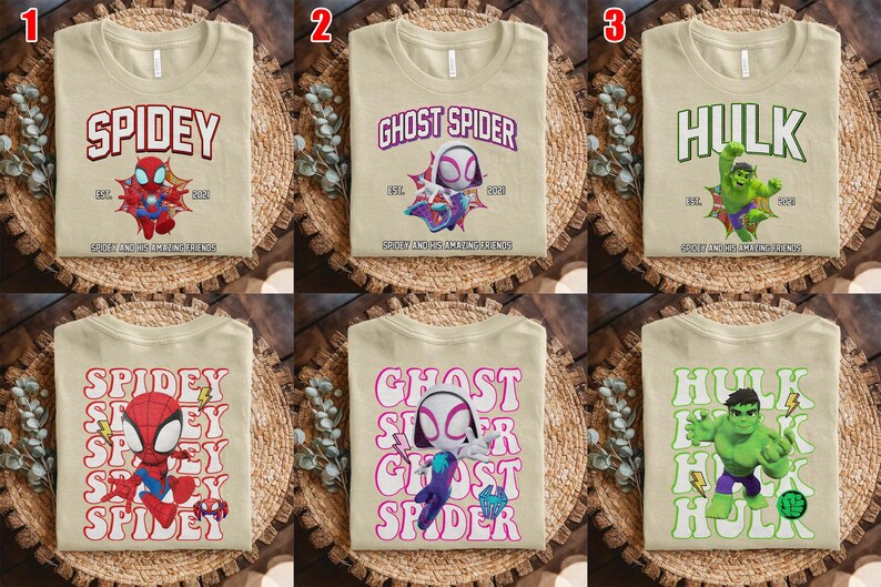 Puede incluir: Camisetas beige con dise&ntilde;os de superh&eacute;roes. Una camiseta presenta "Spidey" con un gr&aacute;fico de Spider-Man, otra dice "Ghost Spider" y la tercera dice "Hulk". Cada camiseta tiene un gr&aacute;fico de superh&eacute;roe diferente.