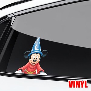 May include: A vinyl decal featuring Mickey Mouse in a sorcerer's outfit. Mickey is wearing a blue hat with stars and a crescent moon, a red robe, and a gold rope belt. The word "VINYL" is printed in red.