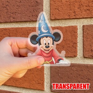 May include: Transparent sticker featuring Mickey Mouse in a sorcerer's outfit. Mickey is wearing a red robe and a blue hat with stars and a crescent moon. The word "TRANSPARENT" is printed in red at the bottom.